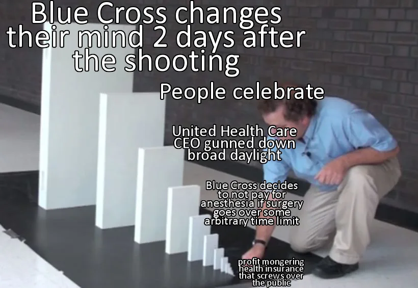 A man in a blue shirt and khaki pants crouches beside a row of white dominoes arranged in descending height on a black floor…