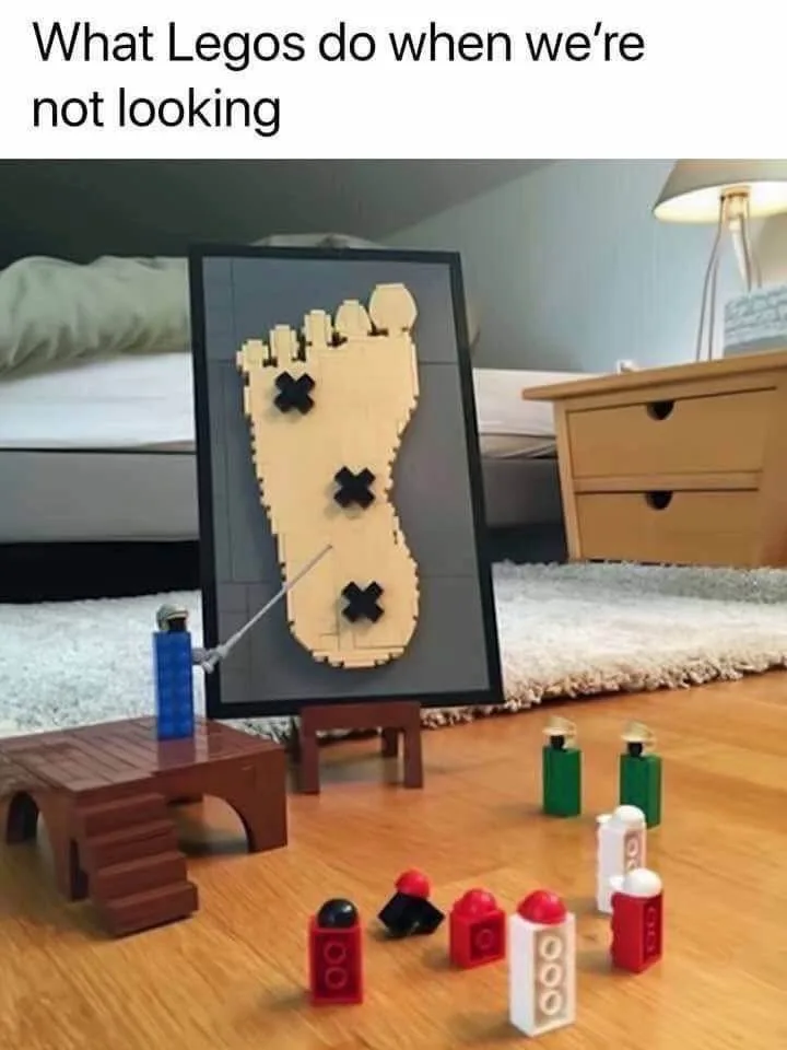 A photo of a bedroom floor with a framed Lego art piece of a human foot with three black X's on it, standing on a small…