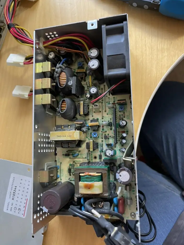 A close-up photo of an open power supply unit on a wooden desk, revealing a circuit board with various electronic…
