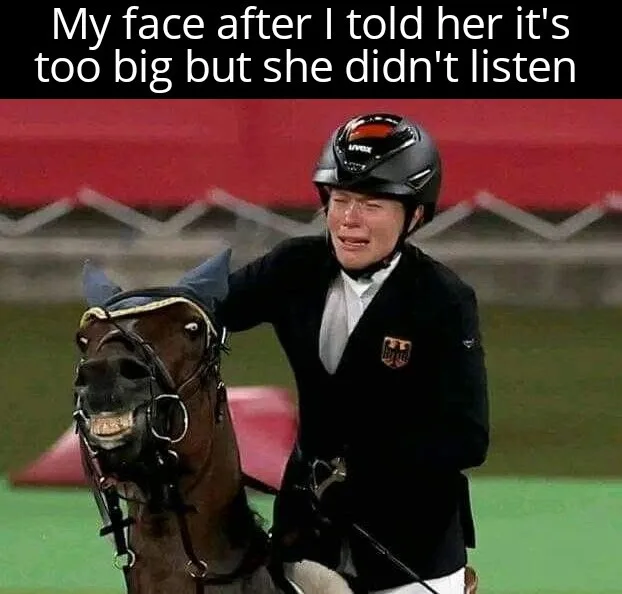 A woman in equestrian gear, wearing a helmet and riding jacket, is visibly crying while holding the reins of a horse. The…