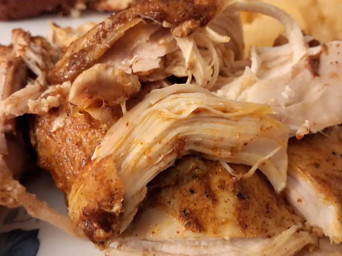 A close-up photo shows shredded, seasoned chicken meat with visible skin and fibers, piled on a plate. The overlaid text…