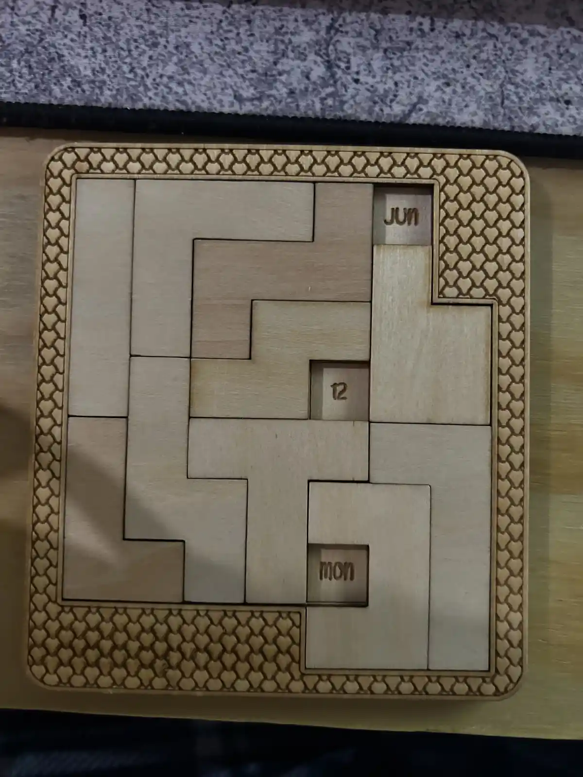 A wooden puzzle calendar with interlocking pieces, showing 'jun' (June) in the top right, '12' in the center, and 'mon'…