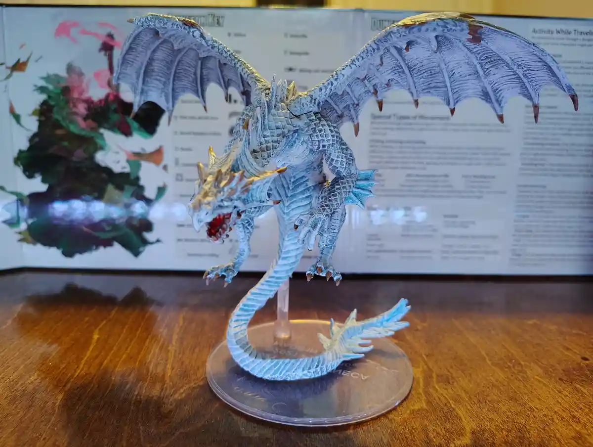 A blue and white painted dragon figurine with spread wings and an open mouth stands on a clear plastic base on a wooden…