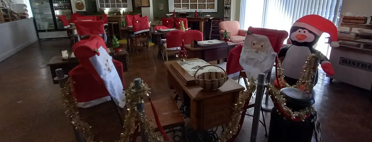 A restaurant decorated for Christmas with chairs covered in red fabric resembling Santa Claus and a penguin wearing a Santa…