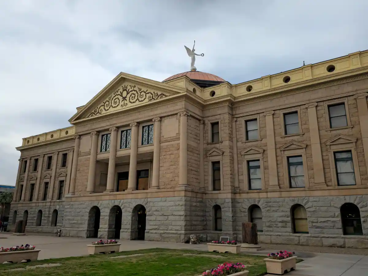 A grand, classical-style stone building with columns and a dome topped by a white angel statue holding a torch and a scroll…