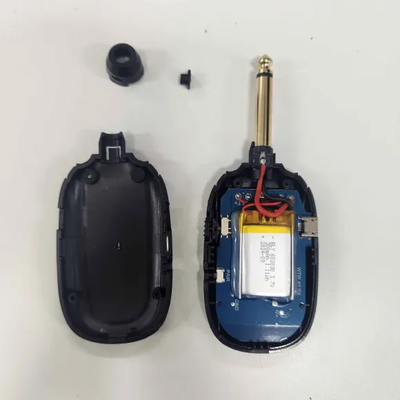 a disassembled black electronic device, likely a remote or small gadget, is shown with its back cover removed. The internal…