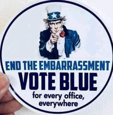 A hand holds a circular political sticker featuring Uncle Sam pointing forward. The sticker has bold blue text reading 'END…