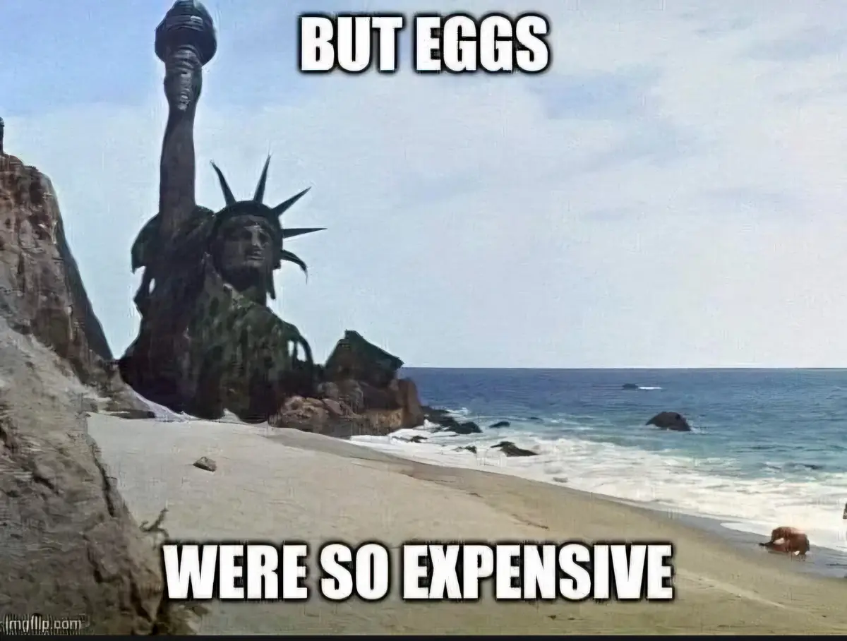 The image shows the Statue of Liberty standing on a beach next to the ocean, with overlaid text reading 'BUT EGGS' at the…