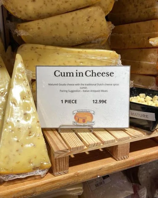 A close-up photo of a cheese display in a grocery store, featuring large wedges of yellow Gouda cheese with visible specks…