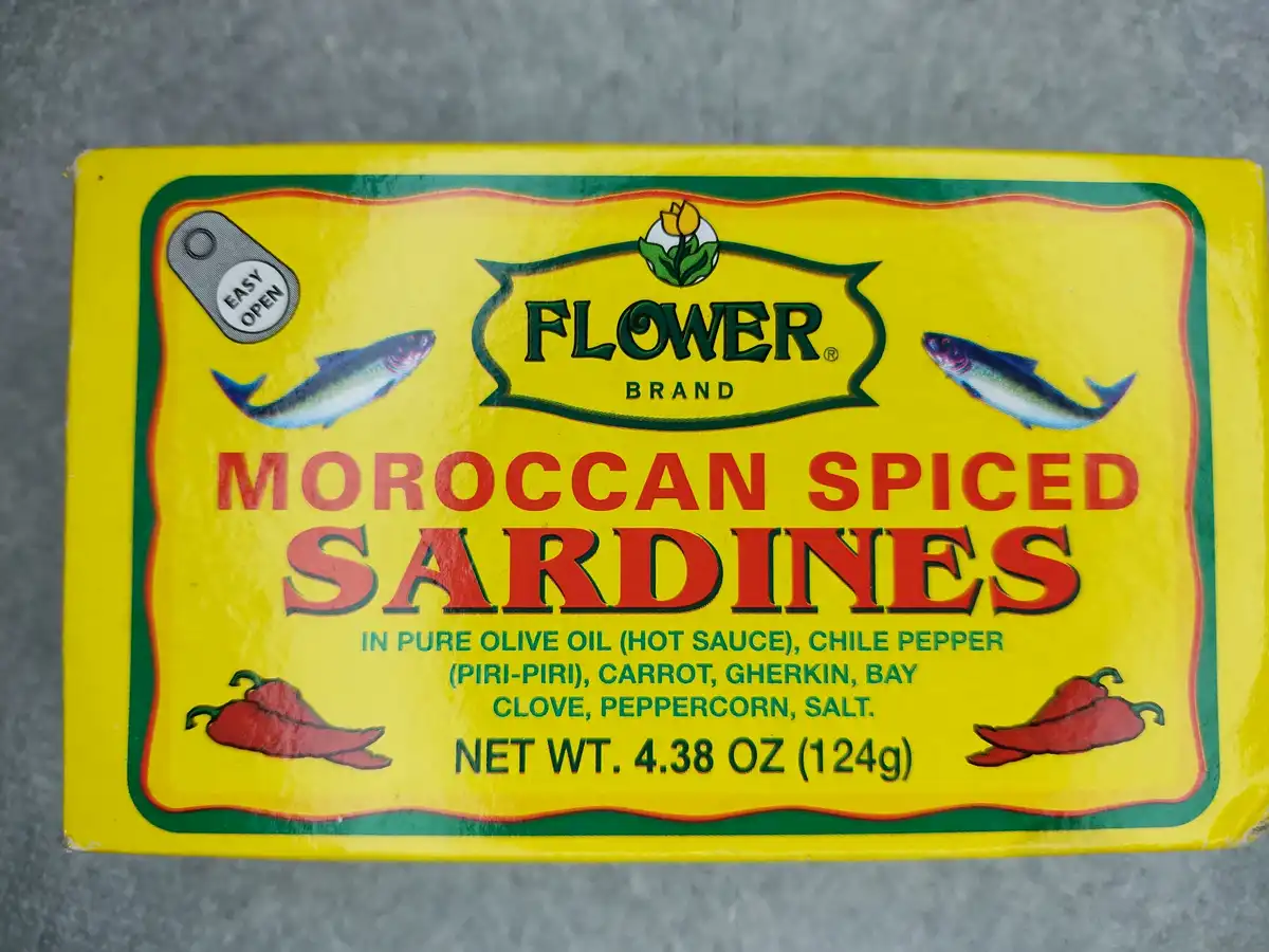 A close-up of a yellow 'Flower Brand' sardine can label showing 'Moroccan Spiced Sardines' with ingredients including 'pure…