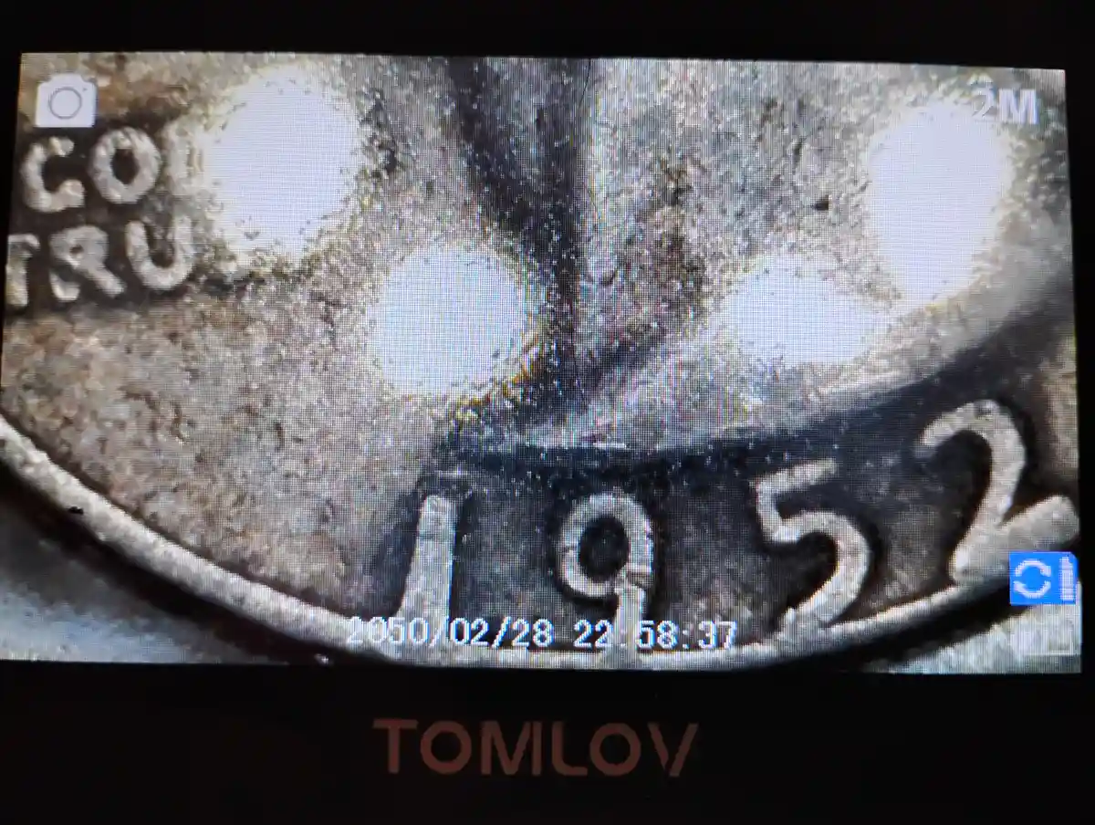 A close-up photo of a worn, metallic coin with the year '1952' visible, overlaid with a timestamp reading '2050/02/28…