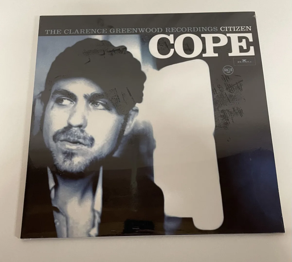 A black-and-white album cover featuring a man with a beard and hat looking off to the side, with a large white silhouette of…