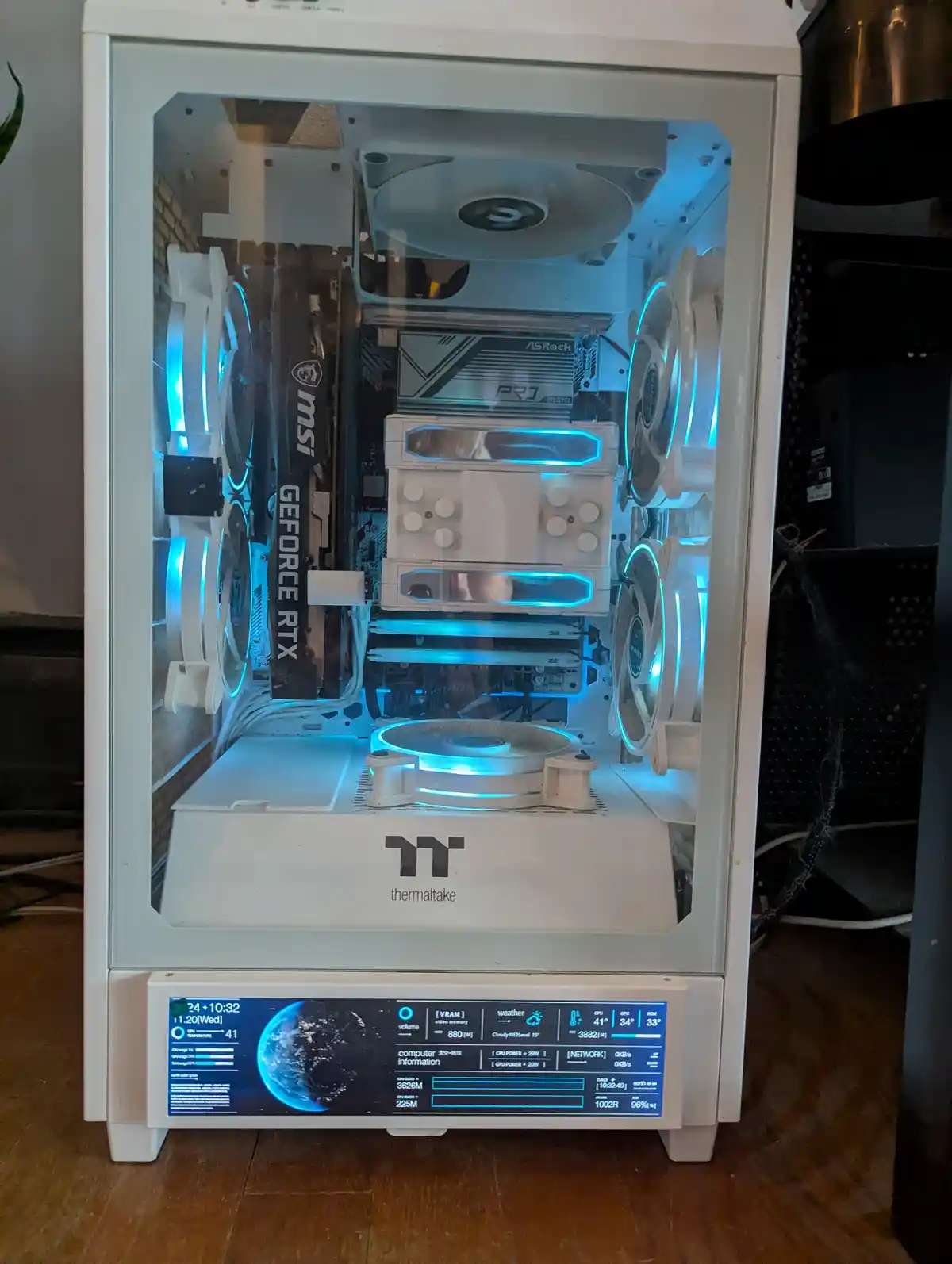 A white Thermaltake computer case with a transparent side panel reveals a meticulously built PC with blue LED lighting on…