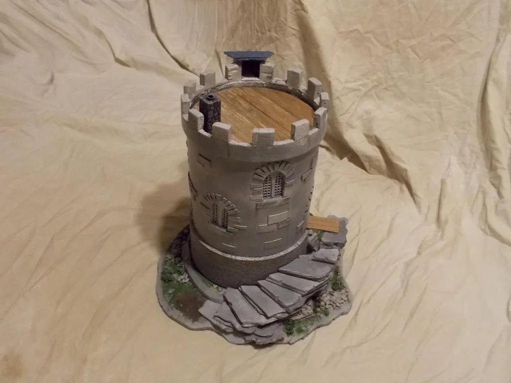 A small, handmade castle model made from a toilet paper roll, painted gray with castle-like details like crenellations…