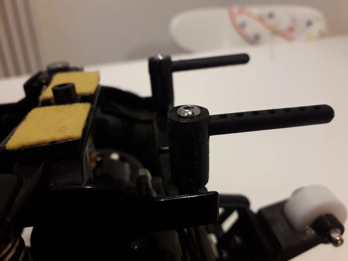 A close-up photo of a black 3D-printed mechanical device, possibly a custom-built RC car or drone part, with visible layer…