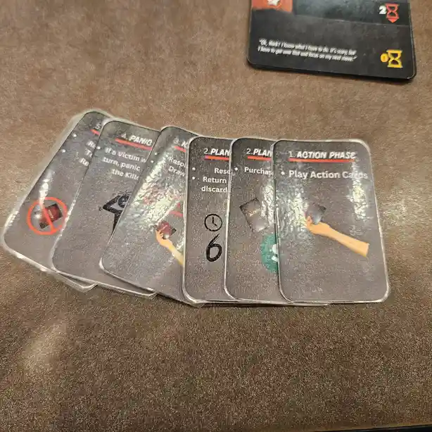 A fanned-out set of translucent game cards from the board game 'Murder!'. The visible cards show phases like 'ACTION PHASE'…