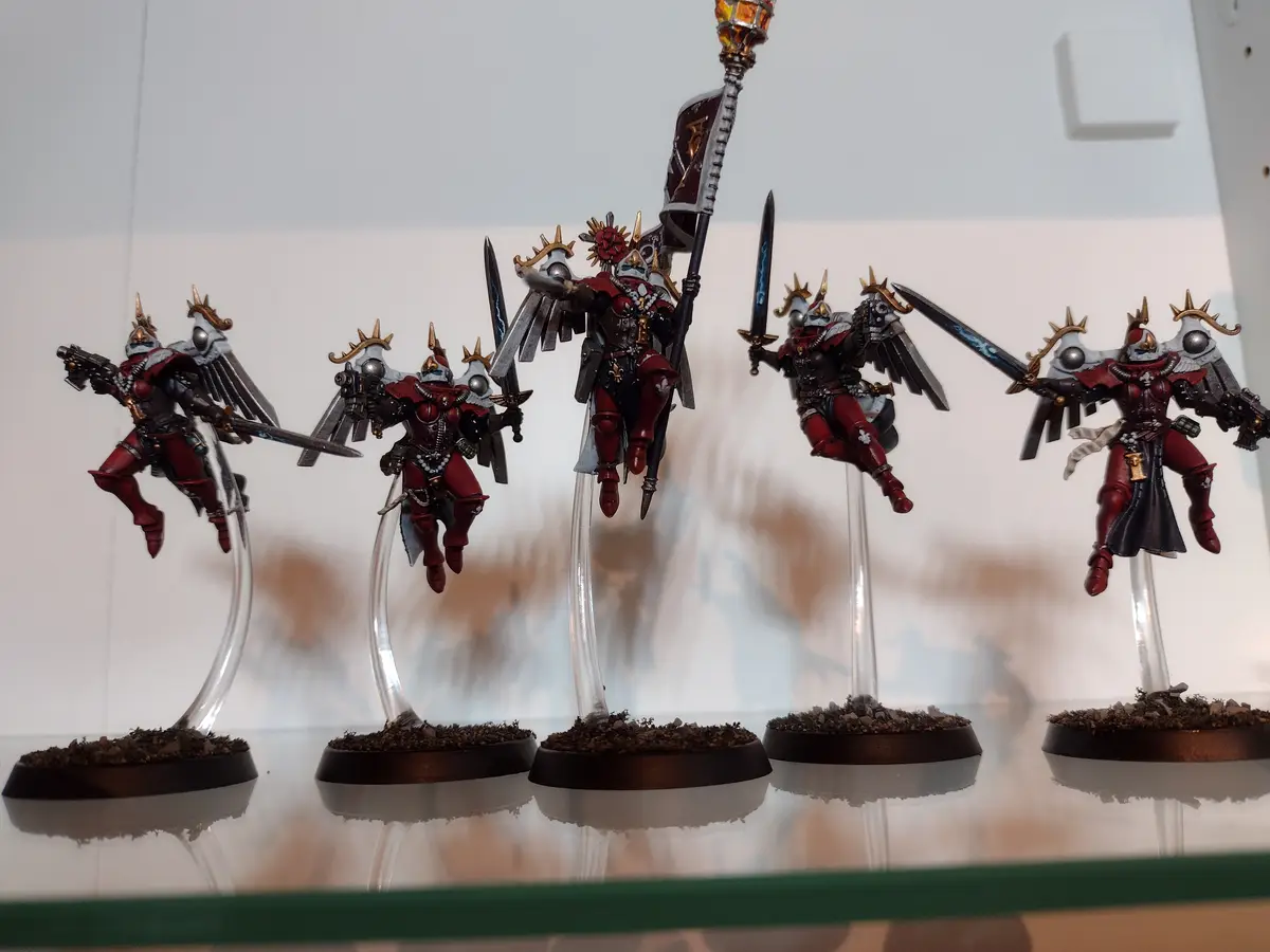 Five intricately painted miniature figurines, resembling winged warriors in red and silver armor, are displayed on clear…