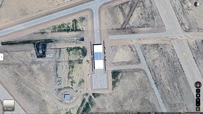a google earth satellite image of a desert airport with runways, taxiways, and hangars, overlaid with the text 'this is not…