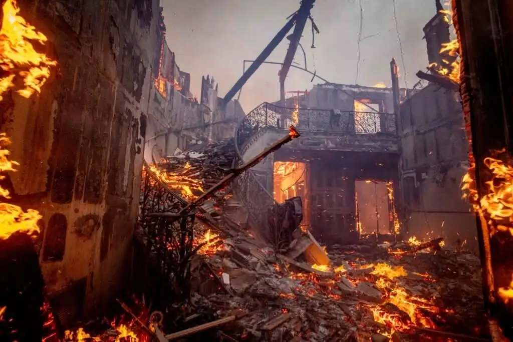 A dramatic image of a building engulfed in flames and rubble, with fire consuming the structure and debris scattered…
