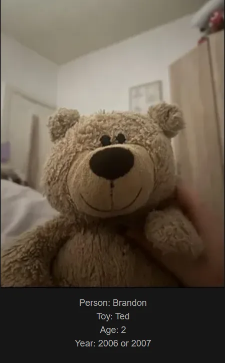 A close-up photo shows a person's hand holding a light brown, fluffy teddy bear with black button eyes and a stitched smile…