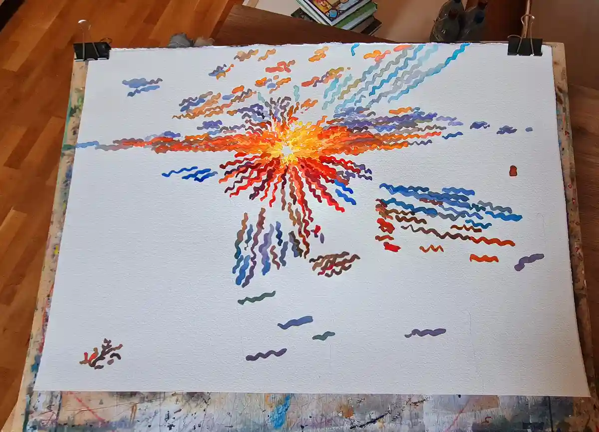 A watercolor painting on white paper, clipped to an easel, depicts a vibrant, explosive burst of orange, red, and blue wavy…
