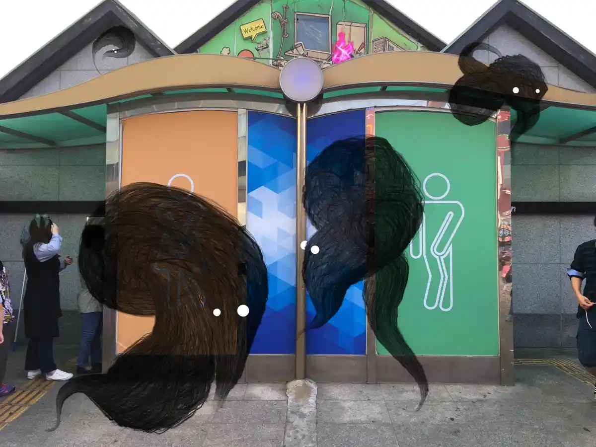 An outdoor public restroom with two stalls, each featuring a gender symbol: a female symbol on the left and a male symbol on…