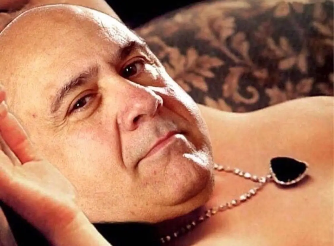 a close-up photo of a bald man, likely Pope Benedict XVI, lying shirtless on a patterned couch, looking directly at the…