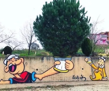 A street mural depicts Pepe Le Pew, a cartoon skunk, extending his leg to hold a potted tree, while a small yellow cat…