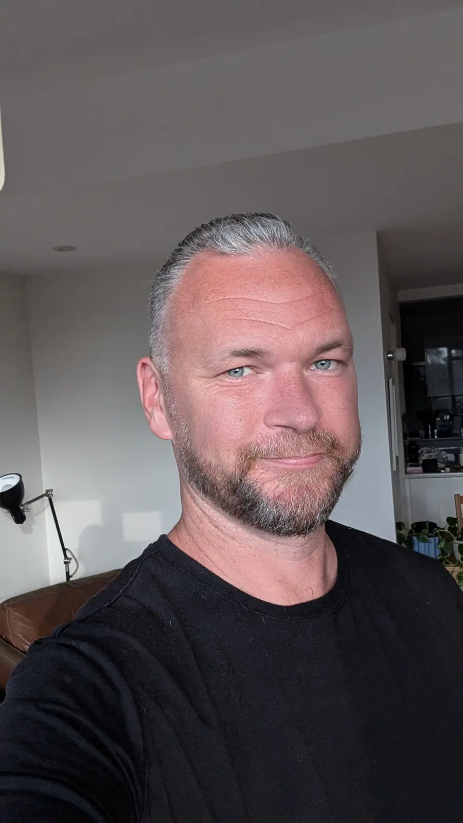 A selfie of a middle-aged man with gray hair and a beard, wearing a black t-shirt, looking at the camera with a slight…