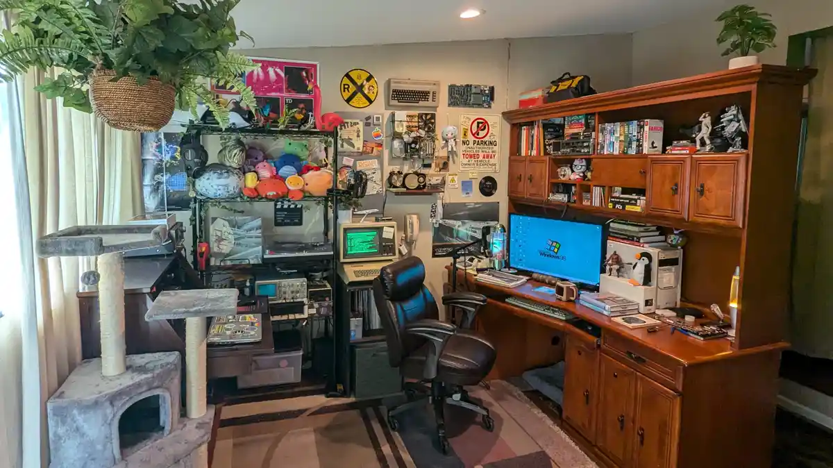 A cluttered home office filled with retro tech like a Windows 98 computer, vintage keyboards, and a lava lamp, surrounded by…