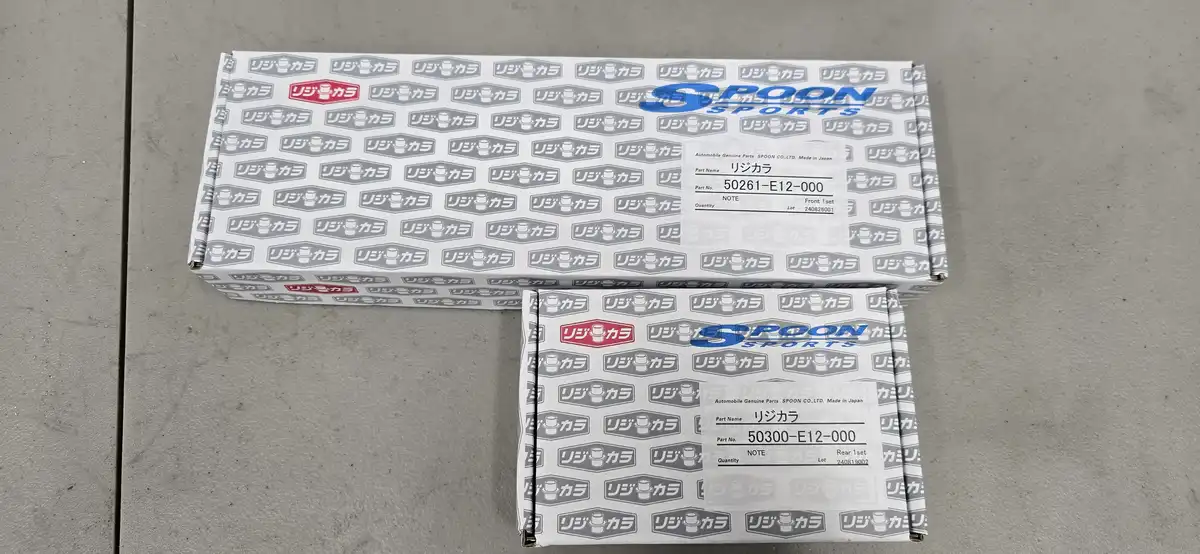 Two identical white boxes with repeating 'リジカラ' logos and 'SPOON SPORTS' branding sit on a gray surface. Each box has a…