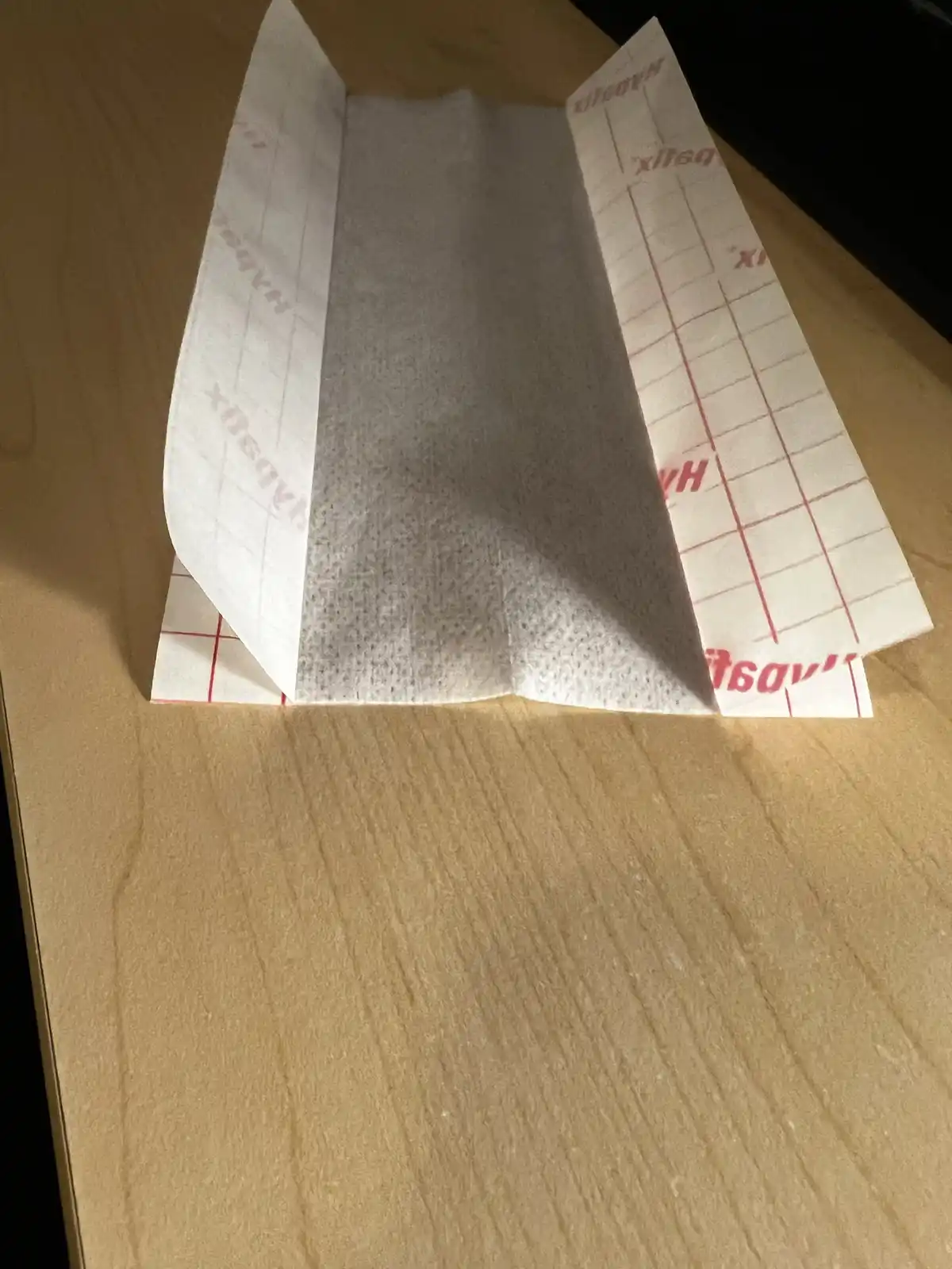 A white paper towel with red grid lines and reversed 'Häagen-Dazs' branding is folded into a triangular shape on a wooden…