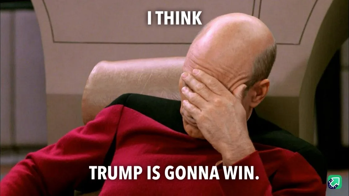 A bald man in a red Starfleet uniform sits in a chair, covering his face with his hand in a gesture of despair or…