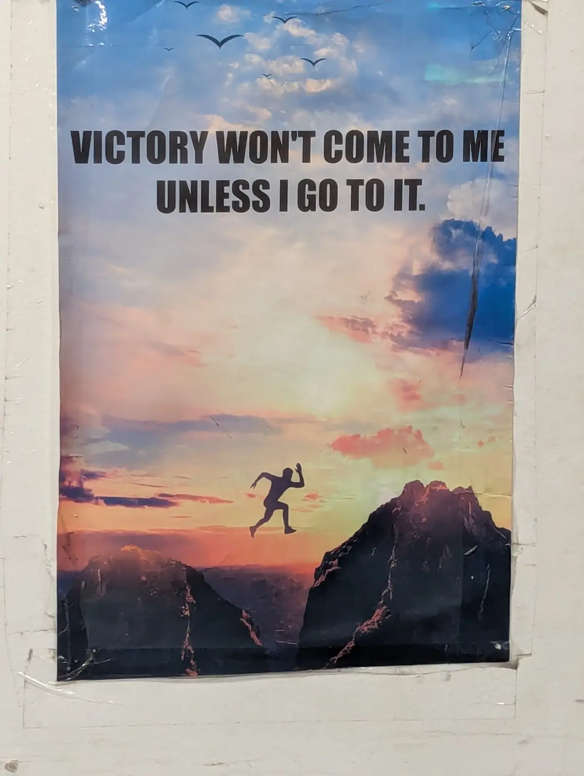 A motivational poster shows a silhouette of a person leaping across a chasm between two mountains under a colorful sunset…