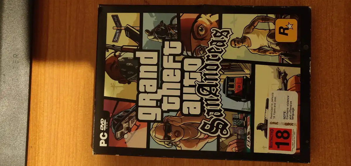 A physical PC DVD-ROM box for the video game Grand Theft Auto: San Andreas, featuring its iconic comic-book style cover art…