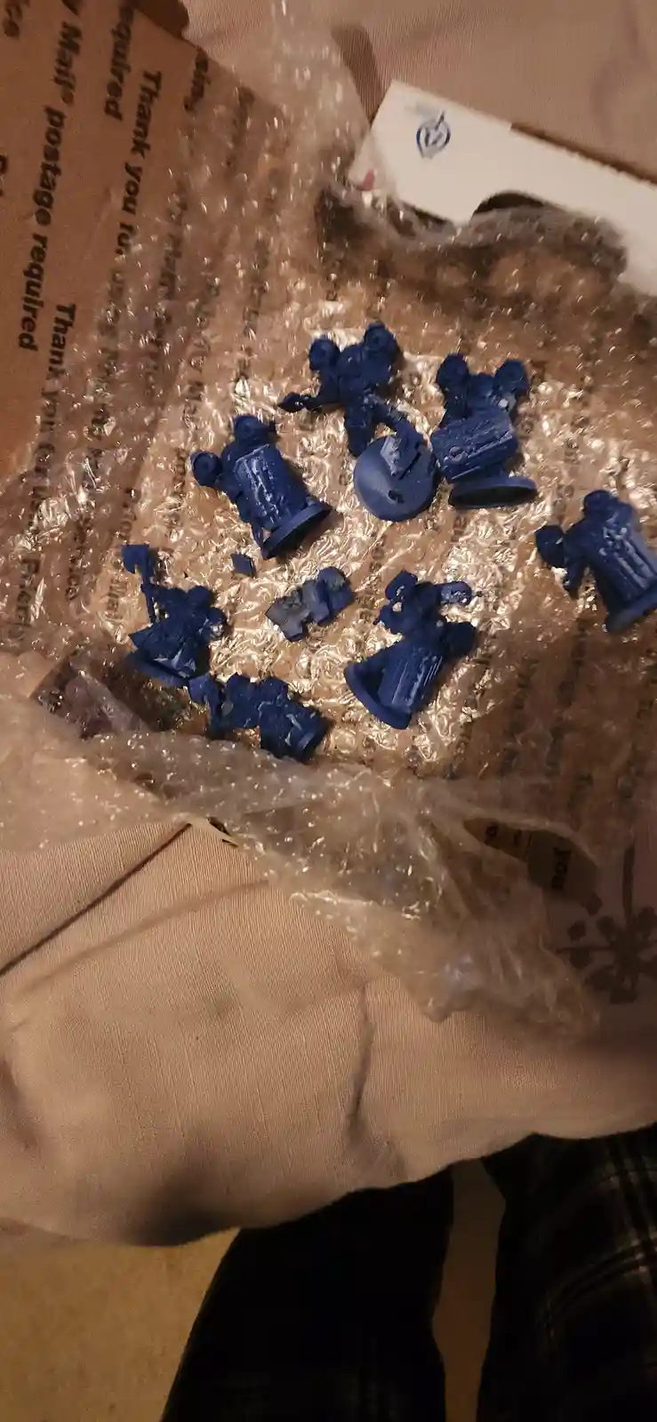A collection of blue-painted miniature figurines, likely for tabletop gaming, are scattered across bubble wrap on a fabric…