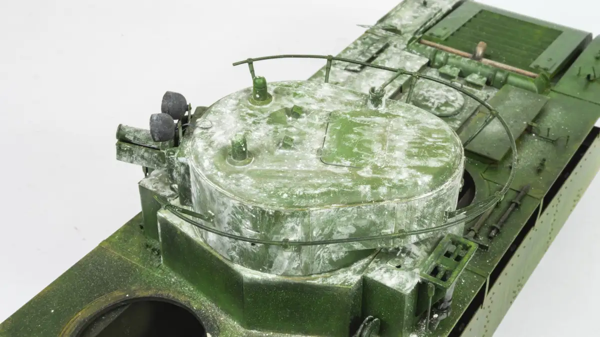 A close-up photo of a green military tank model covered in white dust or powder, with visible details like hatches, rails…