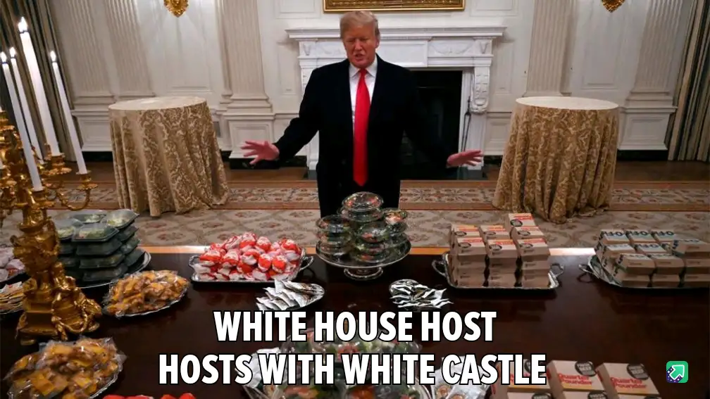 A man in a black suit and red tie stands in an ornate room with a large table in front of him covered with various food…