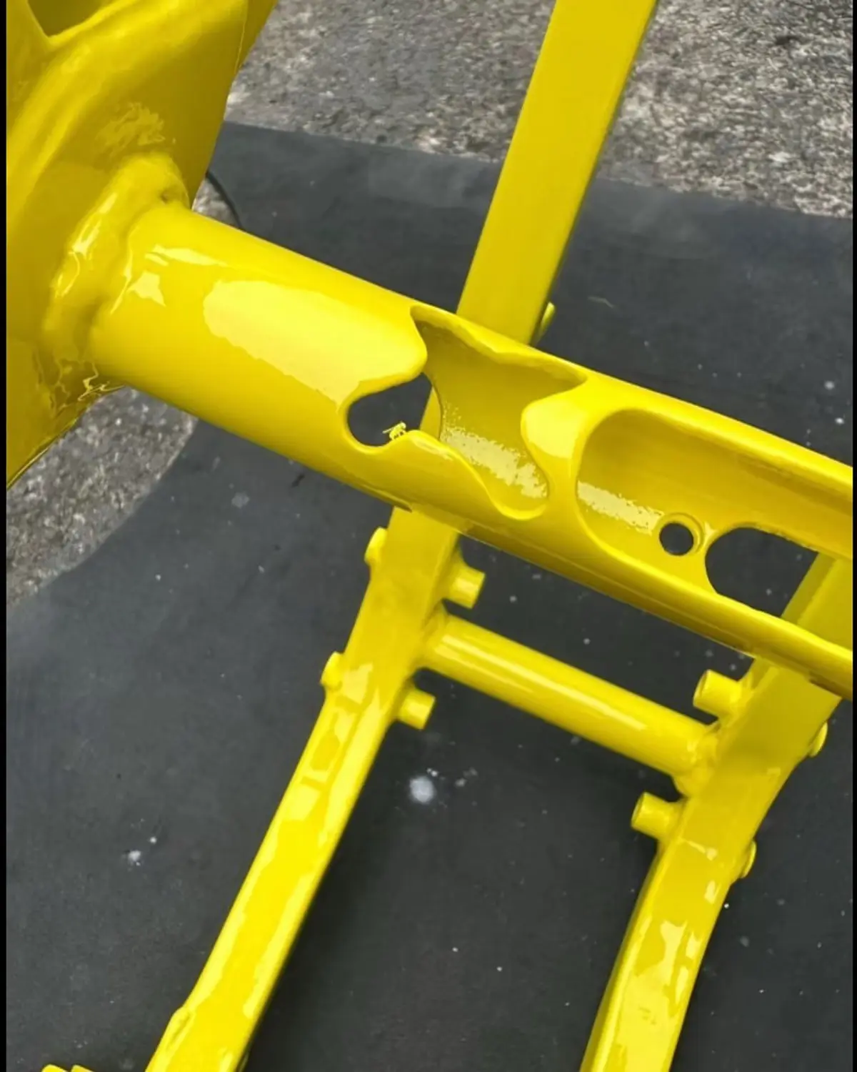 A close-up photo shows a freshly painted, glossy yellow bicycle frame lying on a dark surface, with visible paint drips and…