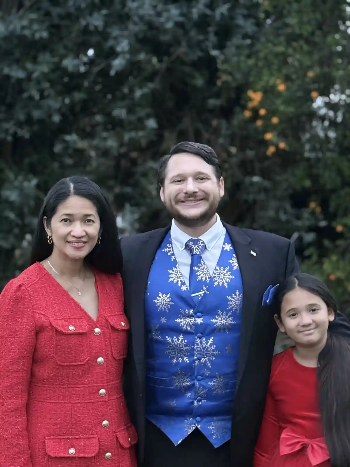 A family photo shows a man in a dark suit wearing a bright blue vest and tie covered in white snowflake patterns, flanked by…