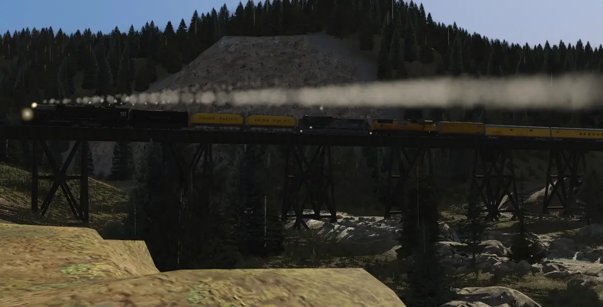 A steam locomotive pulling Union Pacific freight cars crosses a wooden trestle bridge over a rocky, forested valley. A thick…