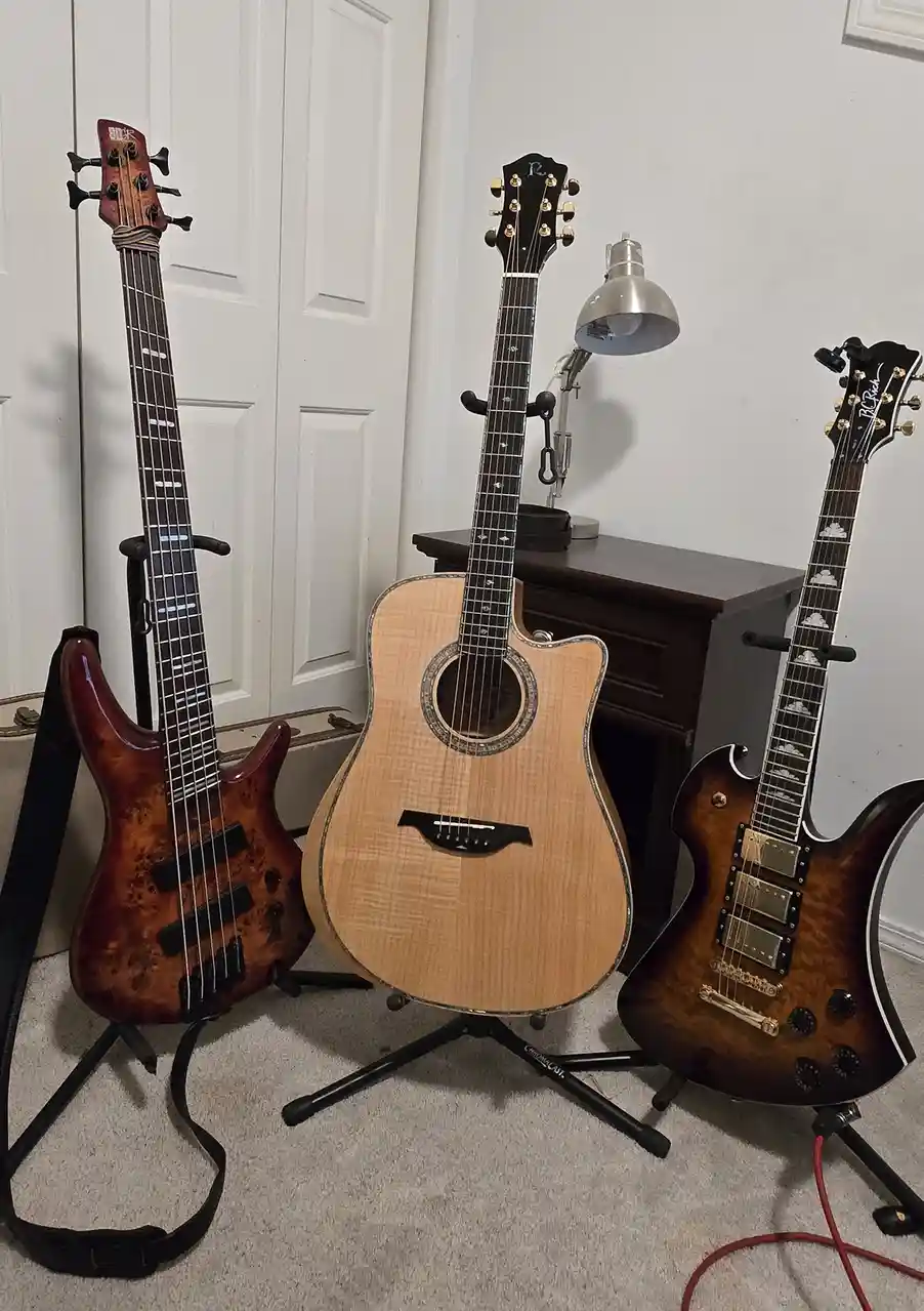 Three stringed instruments — a bass guitar, an acoustic guitar, and an electric guitar — are standing upright on stands in a…