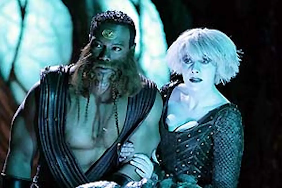 A still from a fantasy film shows a bearded man with a third eye and a woman with short white hair, both looking shocked…