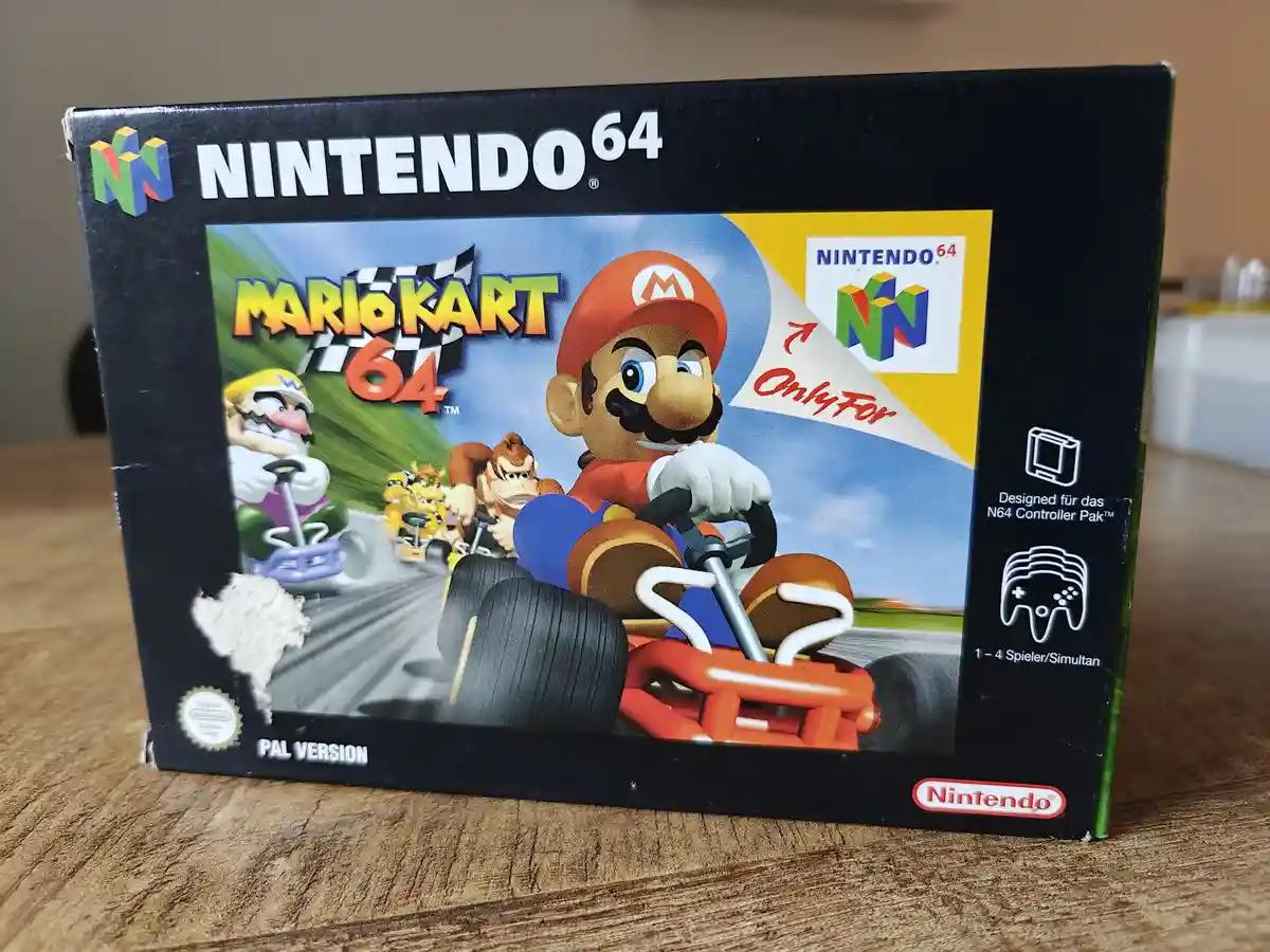 A photo of a physical Nintendo 64 game box for Mario Kart 64, showing Mario in a kart with other characters like Wario and…