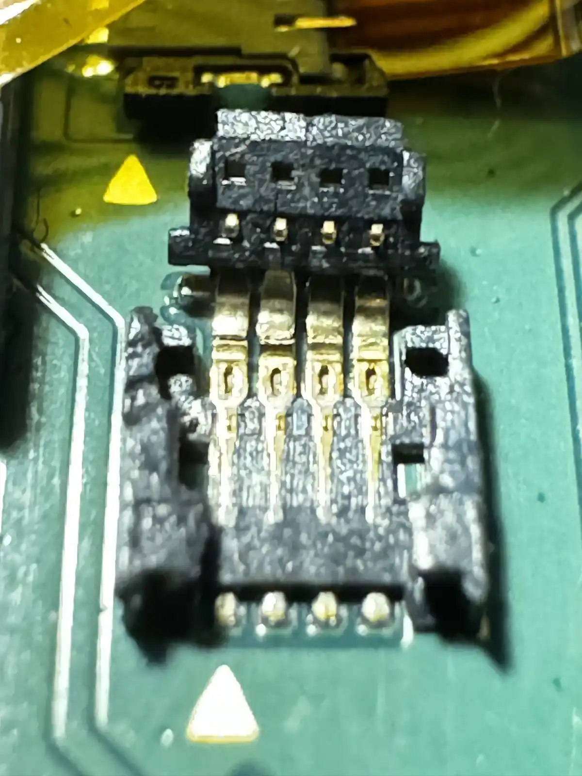 A close-up photo of a damaged electronic connector on a green circuit board, with visible burn marks and melted plastic…