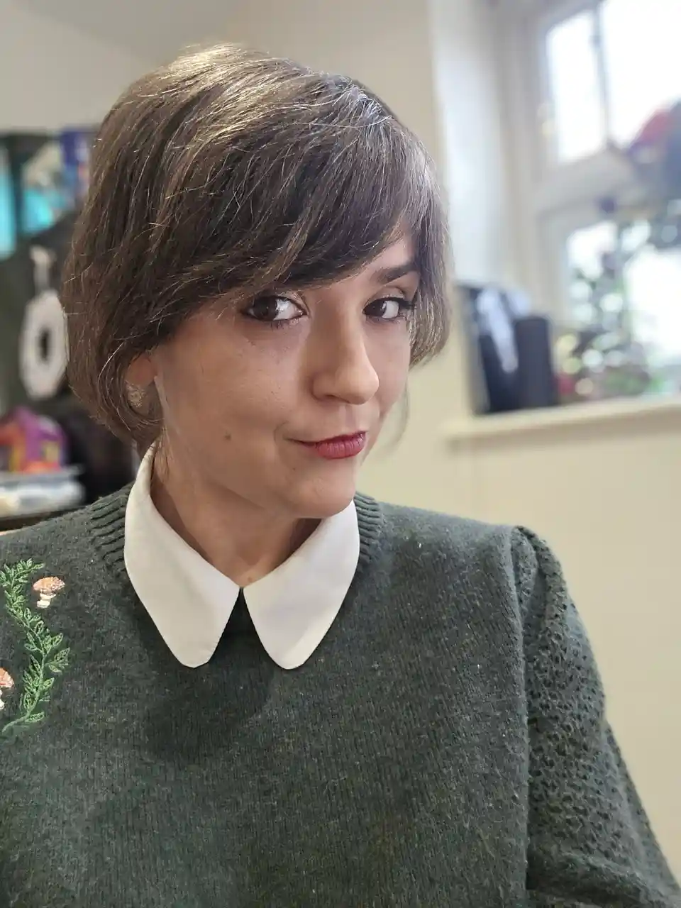 A woman with short brown hair and a white collar sweater looks sideways with a subtle, knowing smirk. The text overlaid on…