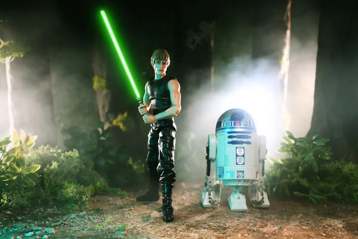 A photo of Star Wars action figures: Luke Skywalker holding a green lightsaber and R2-D2 standing beside him in a misty…