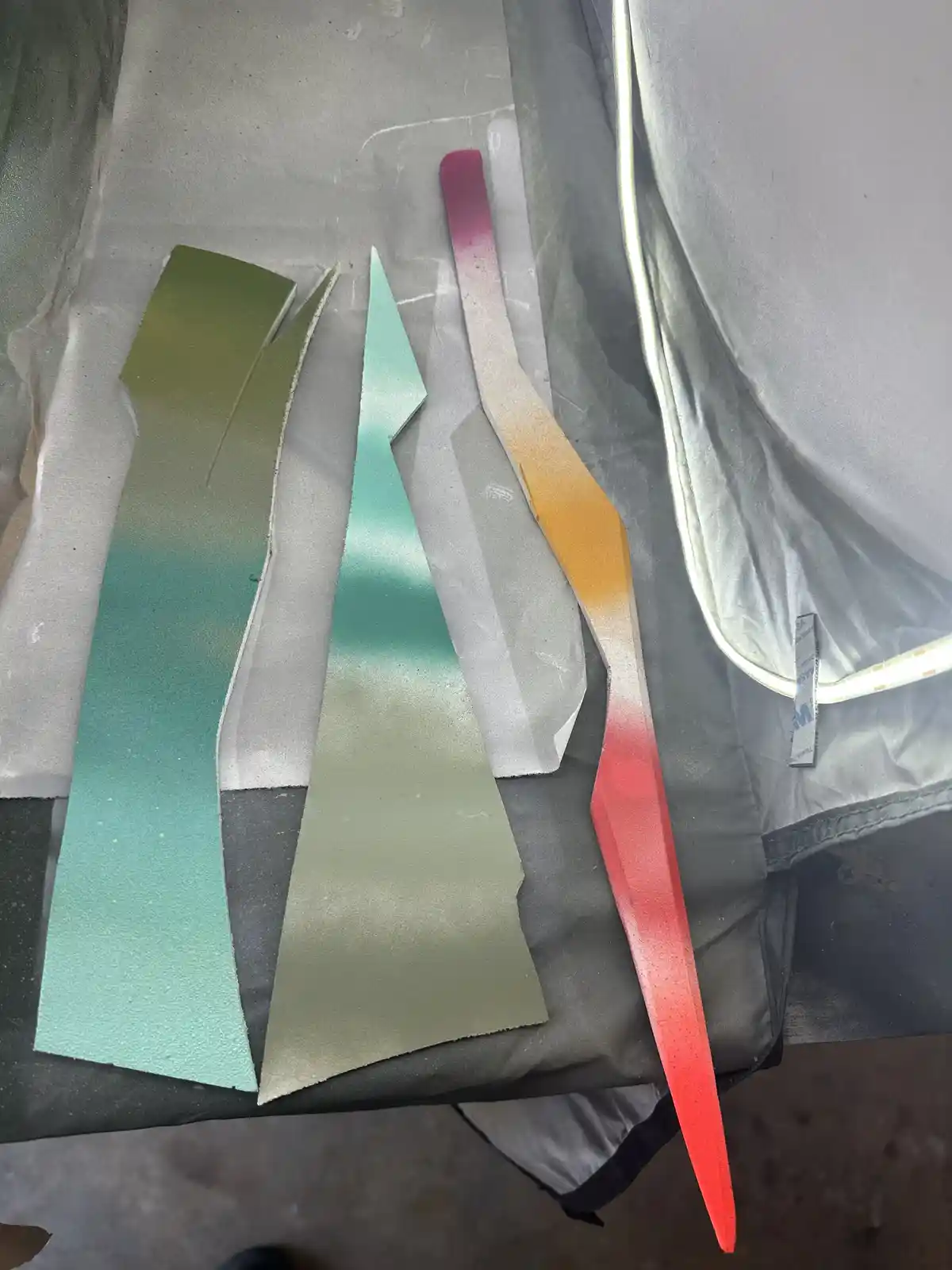 Three irregularly shaped, gradient-painted pieces of material resembling dragon wings lie on a gray fabric surface. The left…
