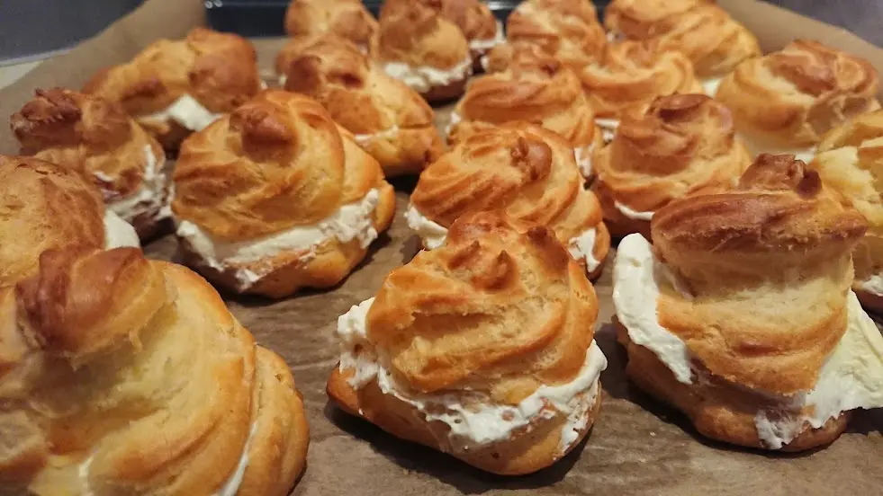 A close-up photo shows numerous golden-brown cream puffs filled with white cream, arranged on parchment paper. The text…