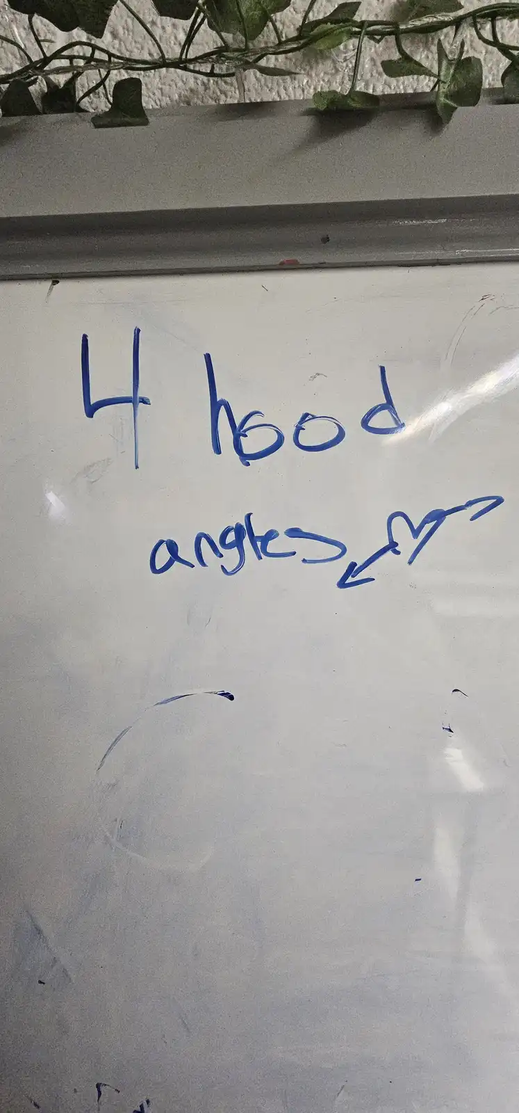 A whiteboard with blue marker handwriting that reads '4 hood angles' with an arrow pointing to the right. The board has some…